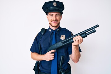 Young caucasian man wearing police uniform holding shotgun winking looking at the camera with sexy...