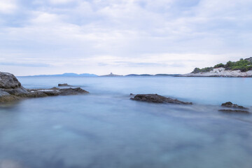 Obraz premium Long exposure photo of Pokonji Dol island with stone lighthouse in the distance, surrounded by silky, adriatic sea surface