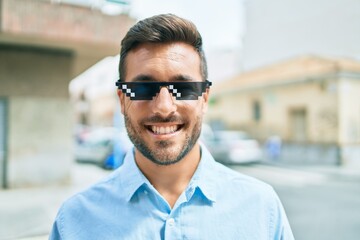 Young hispanic man smiling happy wearing funny sunglasses standing at street of city.