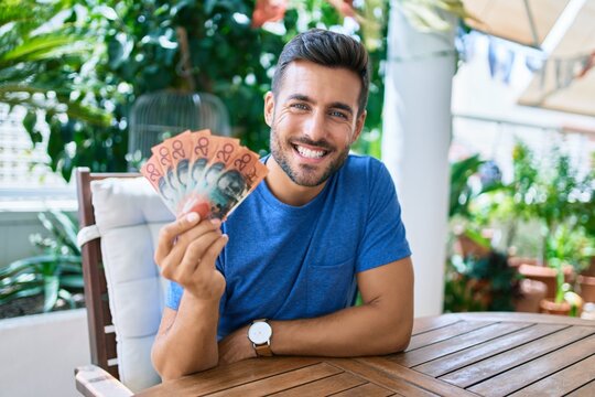 Young hispanic man smiling happy holding australian dollars banknotes at the terrace.