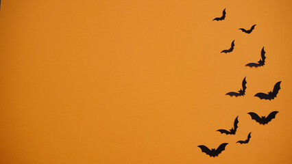 Halloween holiday concept. Black paper bats on bright orange background, top view, flat lay,copy spaes.Celebration of the dead.