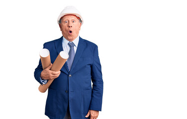 Senior handsome grey-haired man wearing architect hardhat holding blueprints scared and amazed with open mouth for surprise, disbelief face