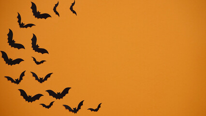 Halloween holiday concept. Black paper bats on bright orange background, top view, flat lay,copy spaes.Celebration of the dead