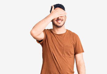 Young hispanic man wearing casual clothes smiling and laughing with hand on face covering eyes for surprise. blind concept.