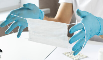 Doctor's hand in gloves holding medical protective mask on white background