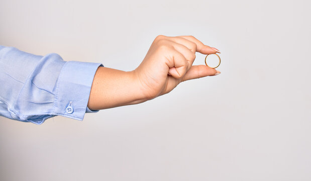 Hand of caucasian young woman holding golden marriage ring over isolated white background