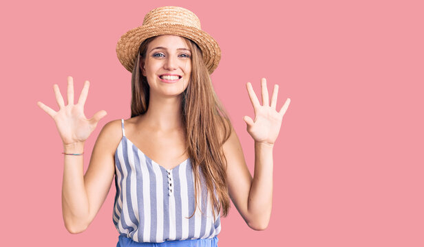 Young beautiful blonde woman wearing summer hat showing and pointing up with fingers number ten while smiling confident and happy.