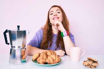 Young redhead woman eating breakfast screaming proud, celebrating victory and success very excited with raised arms