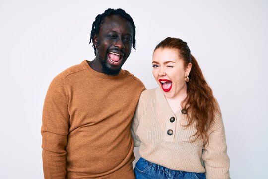 Interracial couple wearing casual clothes winking looking at the camera with sexy expression, cheerful and happy face.