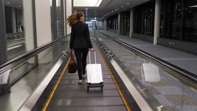 Woman walk on travelator at empty passage of modern airport. Late flight arrive to destination, no other passengers seen around. Moving camera follow behind