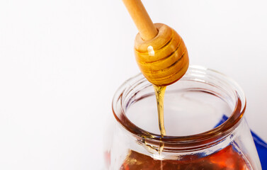 Honey with wooden honey dipper on white background in jar.