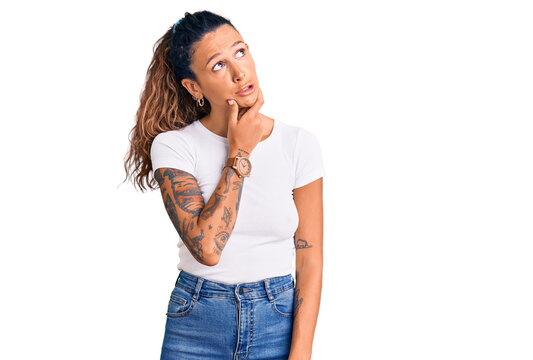 Young hispanic woman with tattoo wearing casual white tshirt thinking worried about a question, concerned and nervous with hand on chin