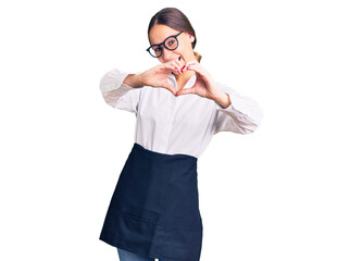 Beautiful brunette young woman wearing professional waitress apron smiling in love doing heart symbol shape with hands. romantic concept.