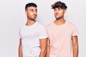 Young gay couple wearing casual clothes smiling looking to the side and staring away thinking.