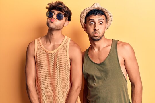 Young gay couple wearing summer clothes puffing cheeks with funny face. mouth inflated with air, crazy expression.