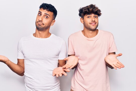 Young gay couple wearing casual clothes clueless and confused expression with arms and hands raised. doubt concept.