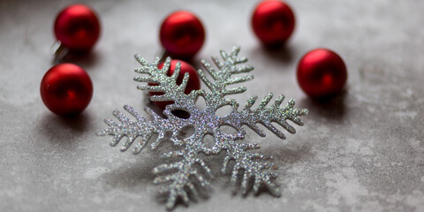 Christmas decorations on a gray background. A silver snowflake surrounded by unfocused burgundy Christmas balls, Christmas toys and stone ornament. Top view.