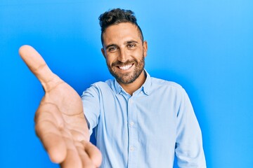 Fototapeta premium Handsome man with beard wearing casual clothes smiling friendly offering handshake as greeting and welcoming. successful business.