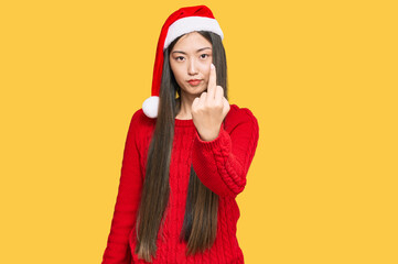 Young chinese woman wearing christmas hat showing middle finger, impolite and rude fuck off expression