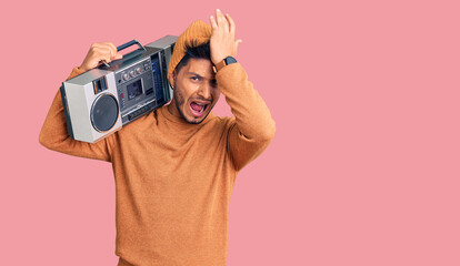 Handsome latin american young man holding boombox, listening to music surprised with hand on head for mistake, remember error. forgot, bad memory concept.