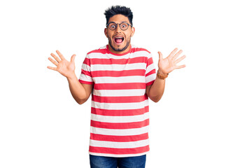Fototapeta premium Handsome latin american young man wearing casual clothes and glasses celebrating crazy and amazed for success with arms raised and open eyes screaming excited. winner concept