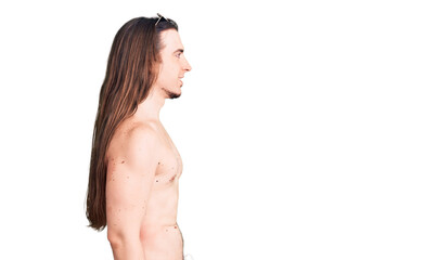 Young adult man with long hair wearing swimwear shirtless looking to side, relax profile pose with natural face with confident smile.