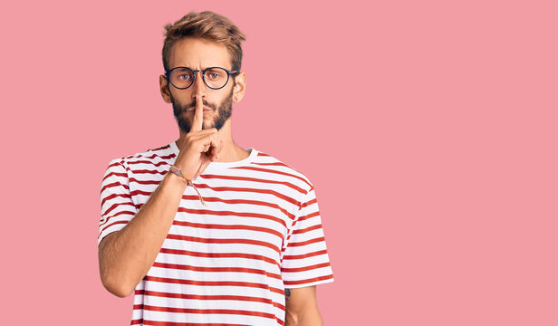 Handsome blond man with beard wearing casual clothes and glasses asking to be quiet with finger on lips. silence and secret concept.