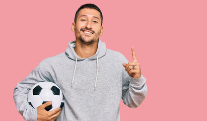 Handsome man with tattoos holding soccer ball surprised with an idea or question pointing finger with happy face, number one