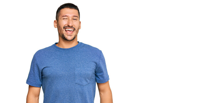 Handsome man with tattoos wearing casual clothes winking looking at the camera with sexy expression, cheerful and happy face.