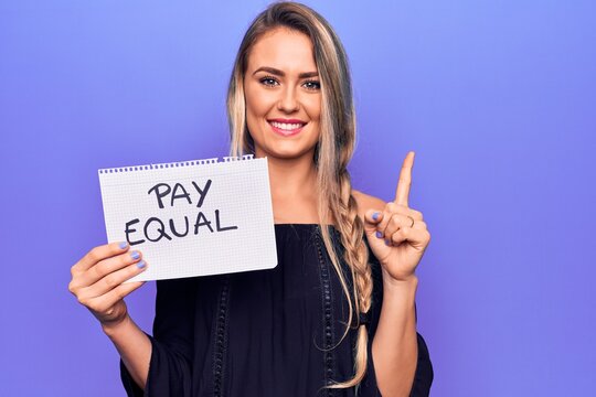 Beautiful blonde woman asking for equality economy holding paper with pay equal message smiling with an idea or question pointing finger with happy face, number one