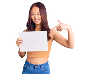 Young beautiful chinese girl holding paper banner with blank space smiling happy pointing with hand and finger