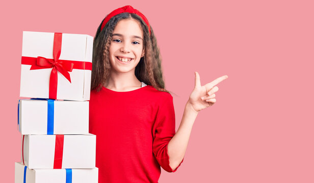 Cute hispanic child girl holding gift smiling happy pointing with hand and finger to the side