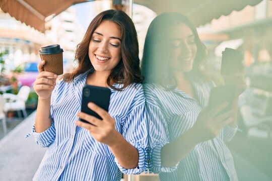 Young hispanic businesswoman using smartphone and drinking take away coffee at the city.