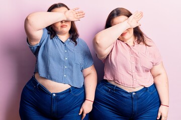 Young plus size twins wearing casual clothes covering eyes with arm, looking serious and sad. sightless, hiding and rejection concept
