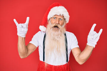 Fototapeta na wymiar Old senior man with grey hair and long beard wearing white t-shirt and santa claus costume shouting with crazy expression doing rock symbol with hands up. music star. heavy concept.
