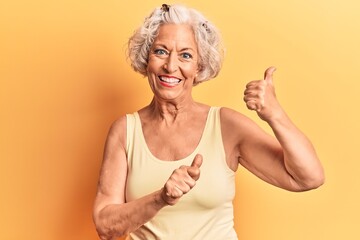 Senior grey-haired woman wearing casual clothes pointing to the back behind with hand and thumbs up, smiling confident