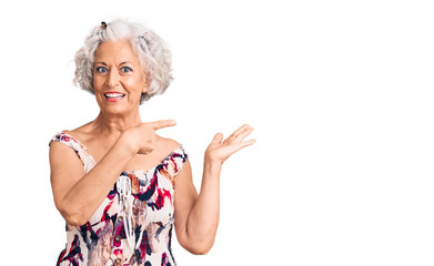 Senior grey-haired woman wearing casual clothes amazed and smiling to the camera while presenting with hand and pointing with finger.