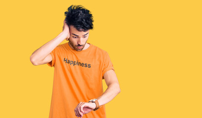 Young hispanic man wearing t shirt with happiness word message looking at the watch time worried,...