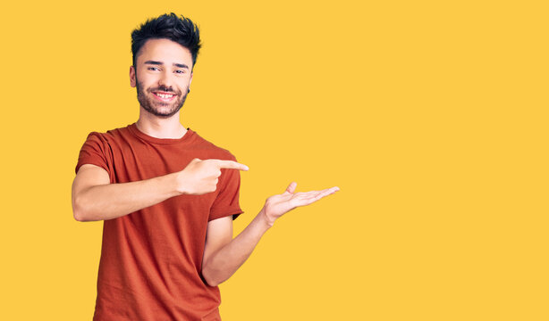 Young hispanic man wearing casual clothes amazed and smiling to the camera while presenting with hand and pointing with finger.