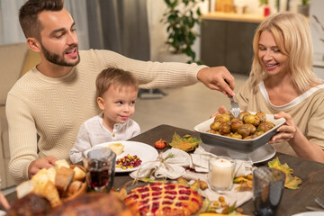 Happy young man with little son on his knees taking baked potato from bowl