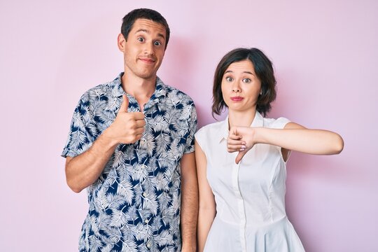 Beautiful couple wearing casual clothes doing thumbs up and down, disagreement and agreement expression. crazy conflict