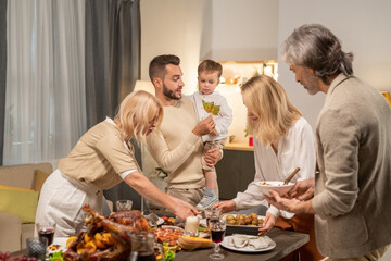 Young man showing dry maple leaf to little son while standing by festive table