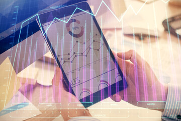 Double exposure of man's hands holding and using a phone and financial graph drawing. Analysis concept.