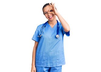 Young beautiful blonde woman wearing doctor uniform and stethoscope doing ok gesture with hand smiling, eye looking through fingers with happy face.