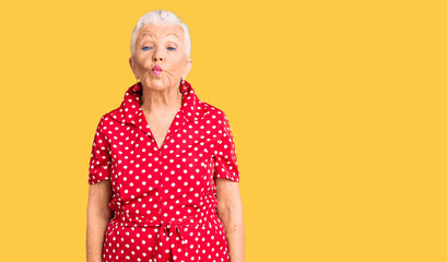 Senior beautiful woman with blue eyes and grey hair wearing a red summer dress making fish face...