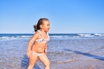Adorable blonde child wearing bikini playing with water at the beach
