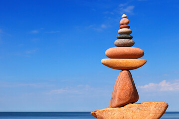 Fototapeta na wymiar A bright Rock zen pyramid of pink pebbles against a blue sky. Concept of Life balance
