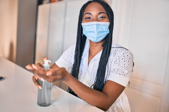 Young african american woman wearing medical mask using sanitizer hand gel at home