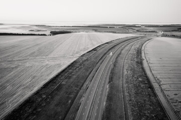 Highway going through meadow in mist surrounded by forest. Aerial view of a road covered in fog.