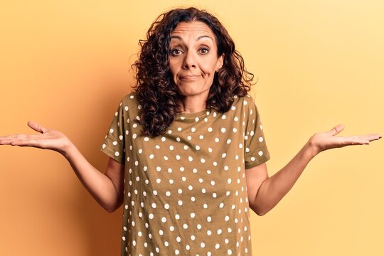 Middle age beautiful woman wearing casual t shirt clueless and confused with open arms, no idea and doubtful face.